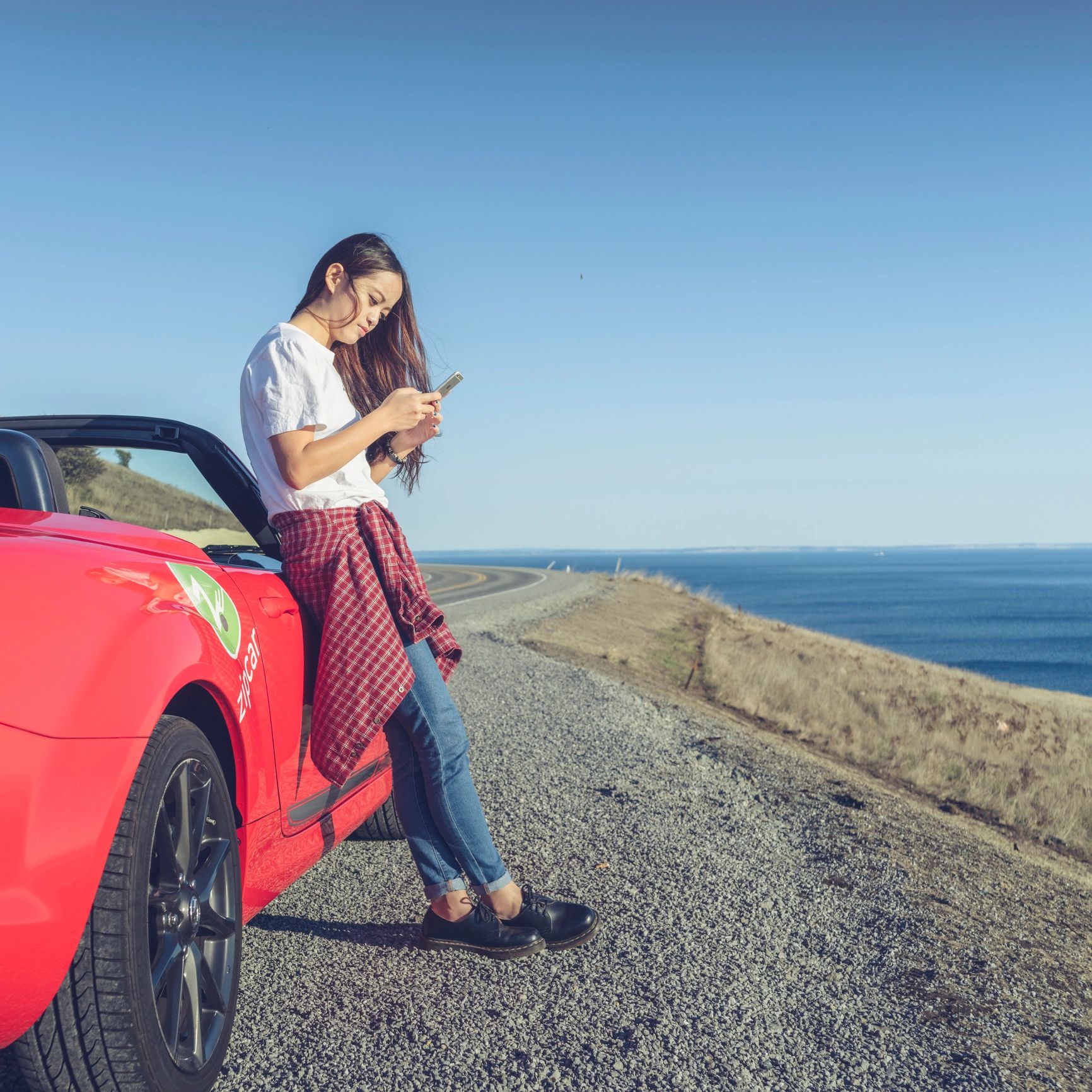 Traveler using smartphone beside a rental car